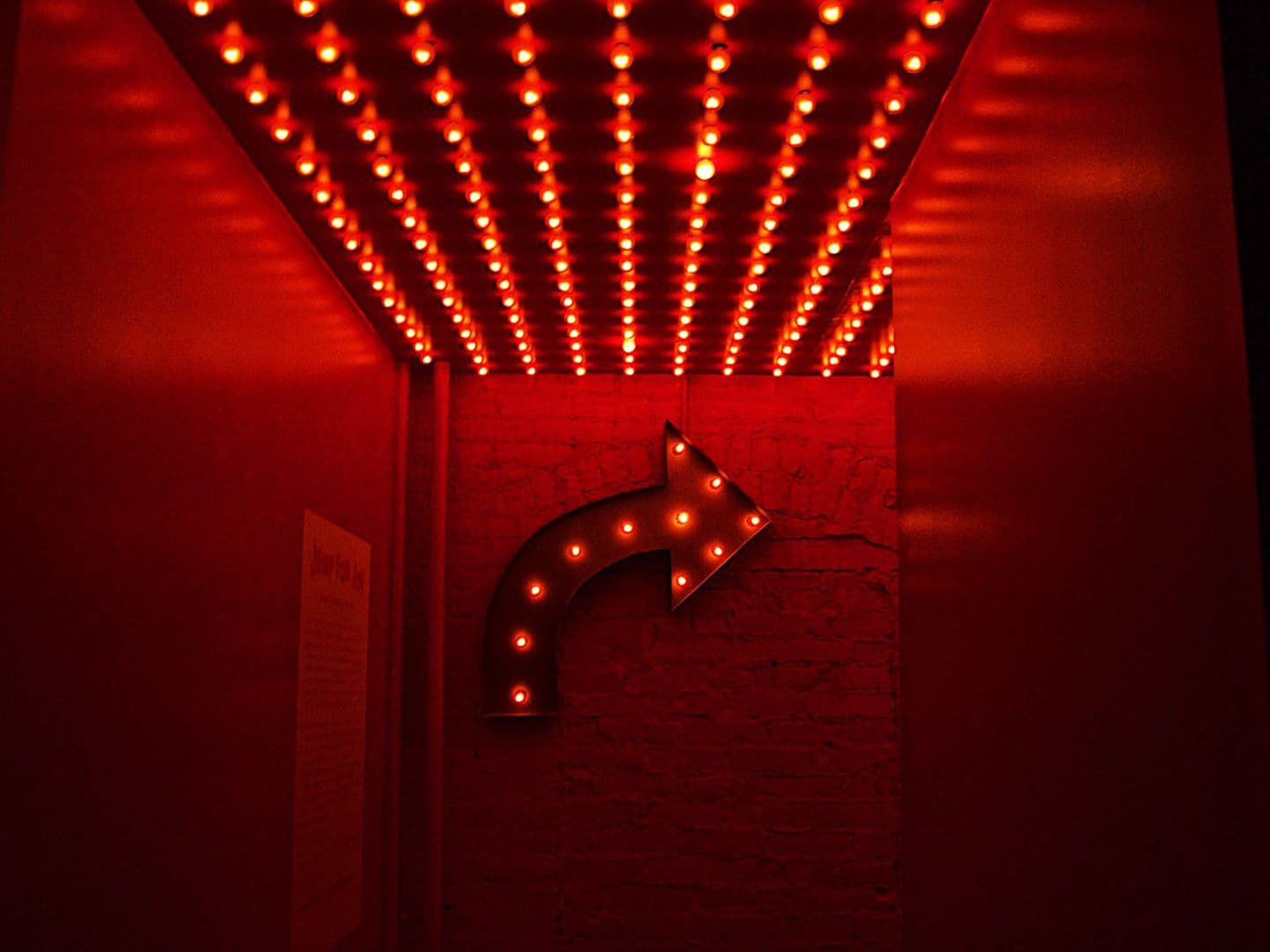 CDCROP: Red lights arrow curve ahead turning a corner hallway (Unsplash)